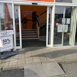 Winkelgevel met glazen deuren, trappen naar ingang, promobord met '50% korting', en personen in de ingang