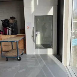 Winkelinterieur met houten tafel op wielen, glazen deur en stellingen met spullen op de achtergrond