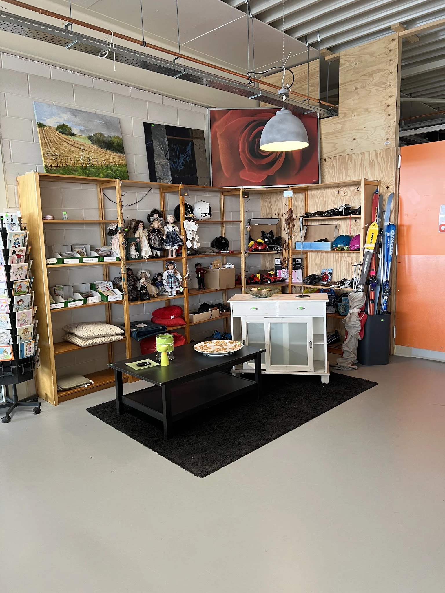 Winkelvloer met houten stellingkasten, zwarte tafel en diverse tweedehands artikelen in een kringloopwinkel