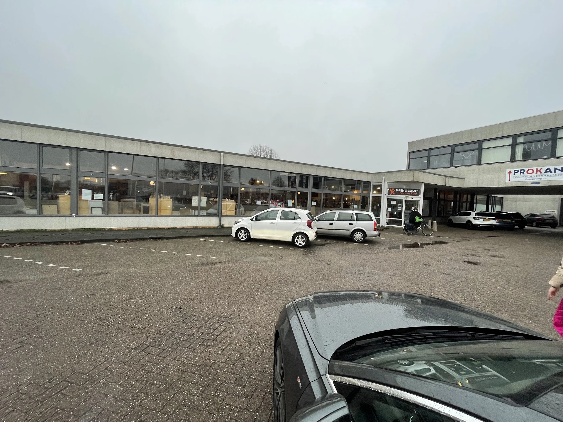Voorgevel van kringloopwinkel met parkeerplaats en witte auto's ervoor
