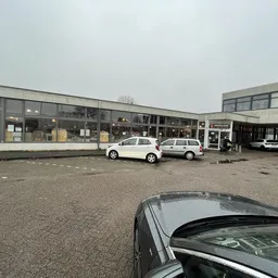 Voorgevel van kringloopwinkel met parkeerplaats en witte auto's ervoor