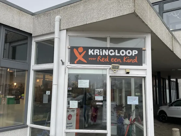 Winkelpui van kringloopwinkel met wit kozijn en oranje logo met tekst 'KRINGLOOP voor Red een Kind' op de gevel