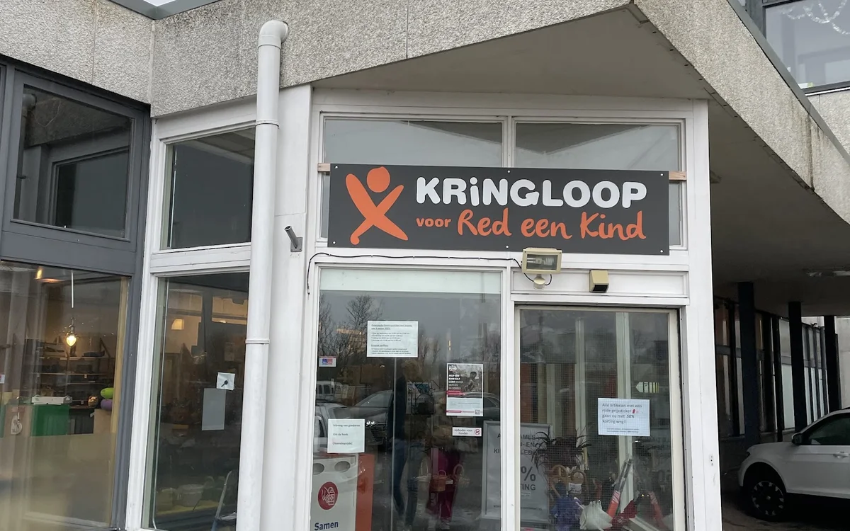 Winkelpui van kringloopwinkel met wit kozijn en oranje logo met tekst 'KRINGLOOP voor Red een Kind' op de gevel