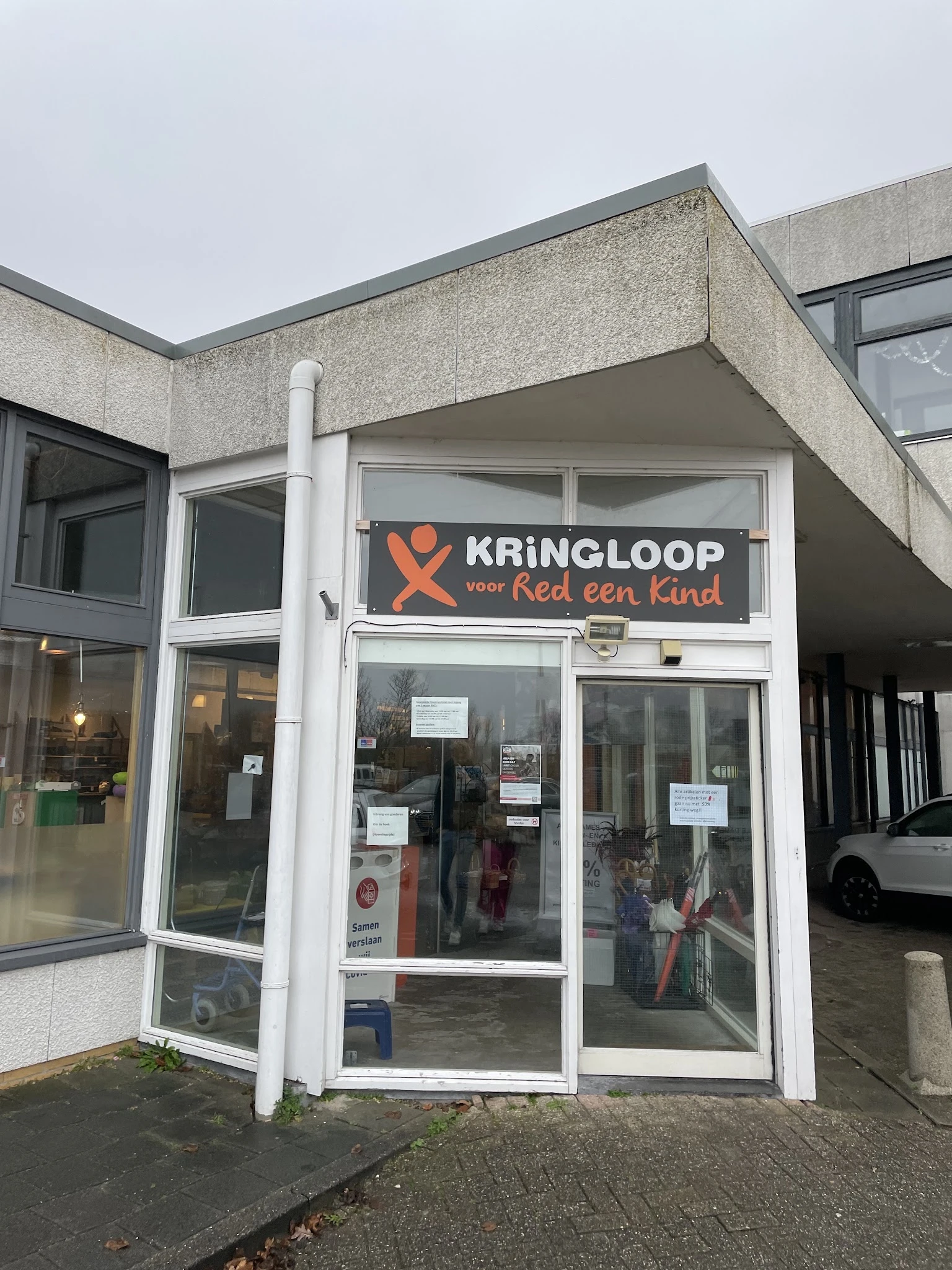 Winkelpui van kringloopwinkel met wit kozijn en oranje logo met tekst 'KRINGLOOP voor Red een Kind' op de gevel
