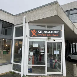 Winkelpui van kringloopwinkel met wit kozijn en oranje logo met tekst 'KRINGLOOP voor Red een Kind' op de gevel