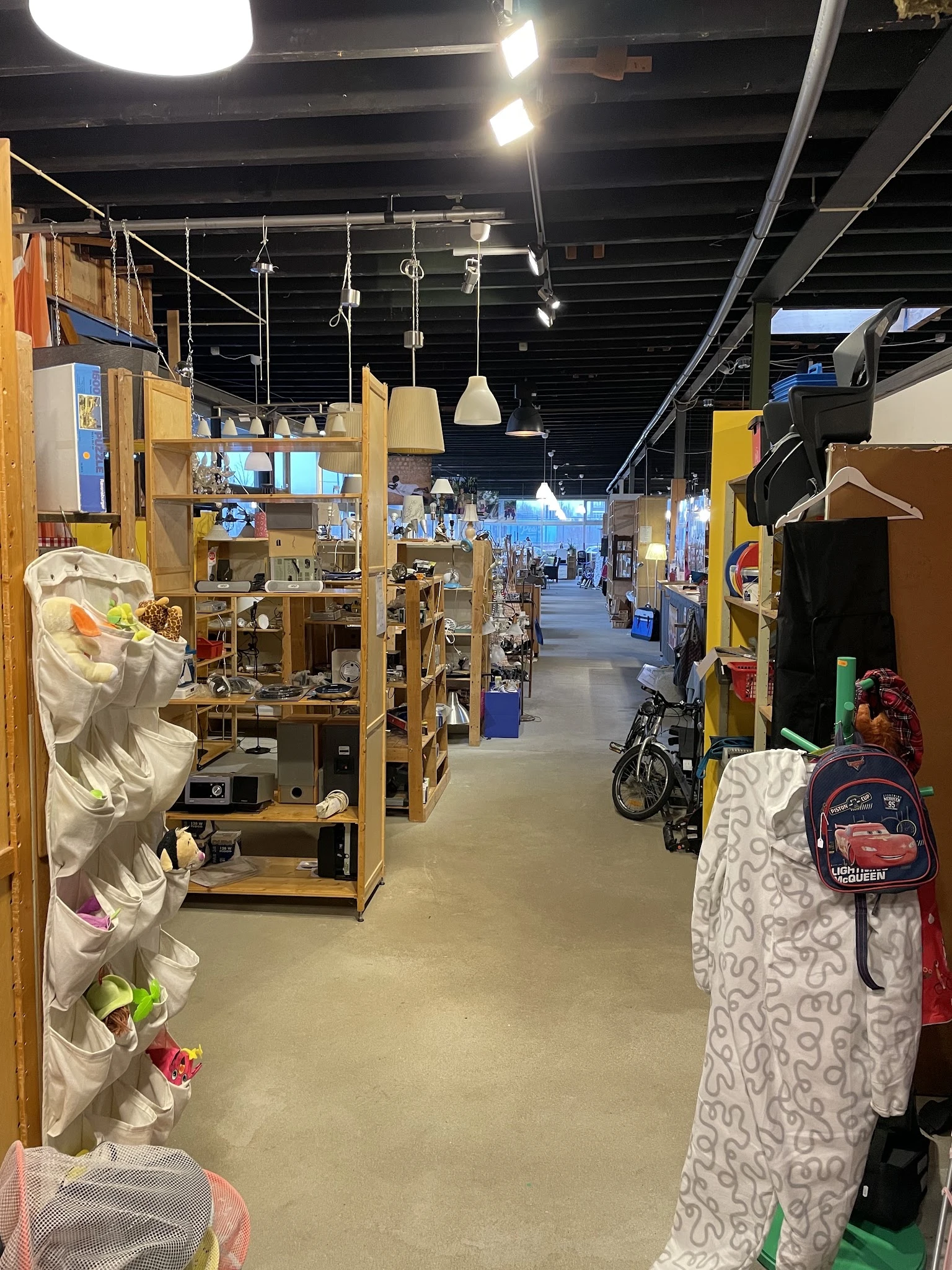 Winkelvloer van kringloopwinkel met houten stellingen, toonkasten en diverse tweedehands spullen langs het gangpad