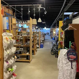 Winkelvloer van kringloopwinkel met houten stellingen, toonkasten en diverse tweedehands spullen langs het gangpad