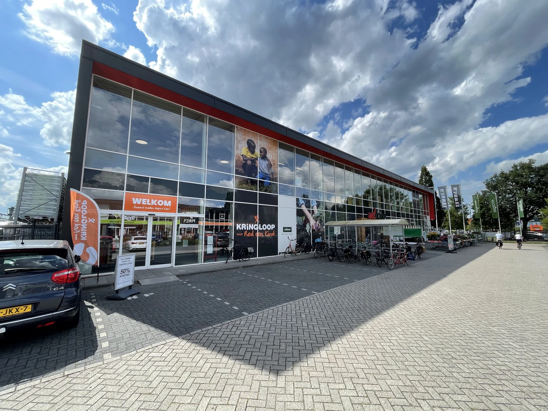 Moderne gevel van kringloopwinkel met grote glazen pui, welkomstteken en ingang aan de Peizerweg
