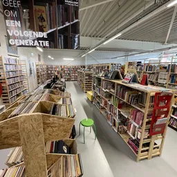 Ruime winkelruimte met kasten en stellingen vol cd's, dvd's en boeken, groen stoeltje zichtbaar