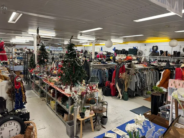 Winkelvloer van kringloopwinkel met kledingrekken, decoraties en ingerichte sectie met kerstversiering en huishoudelijke arti