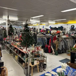Winkelvloer van kringloopwinkel met kledingrekken, decoraties en ingerichte sectie met kerstversiering en huishoudelijke arti