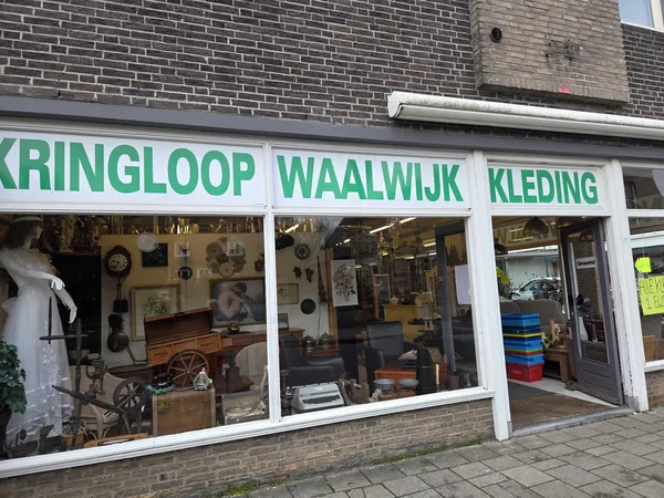 Winkelgevel met drie grote ramen, witte raamkozijnen en groene letters. Zichtbaar zijn verschillende tweedehands spullen in d