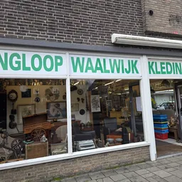 Winkelgevel met drie grote ramen, witte raamkozijnen en groene letters. Zichtbaar zijn verschillende tweedehands spullen in d