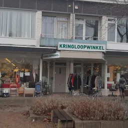 Gevel van kringloopwinkel met winkelnaam KRINGLOOPWINKEL op de pui, etalage met spullen en kleding zichtbaar