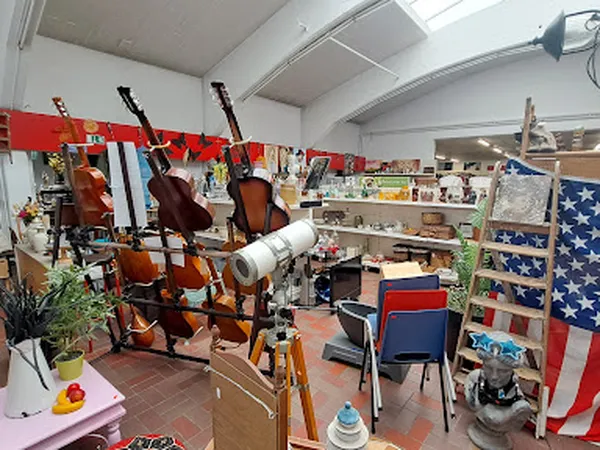 Muziekkamer in kringloopwinkel met violen, cello's, drums en diverse andere instrumenten, stellingen met artikelen op achterg