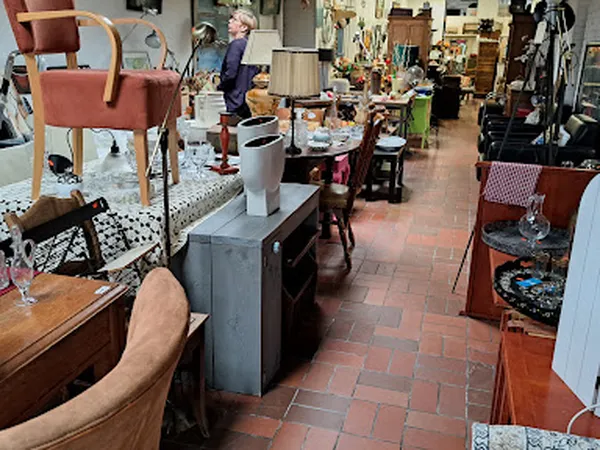 Binnenaanzicht van kringloopwinkel met diverse meubelstukken, stoelen, kasten en gebruiksartikelen uitgestald op een bakstene