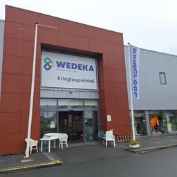 Voorgevel van kringloopwinkel met rood metselwerk en groot WEDEKA-logo met tekst Kringloopwinkel