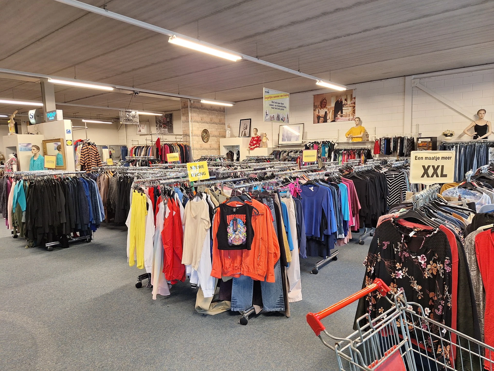 Winkelvloer met meerdere rekken vol tweedehands kleding in verschillende kleuren, onder TL-verlichting
