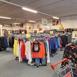Winkelvloer met meerdere rekken vol tweedehands kleding in verschillende kleuren, onder TL-verlichting