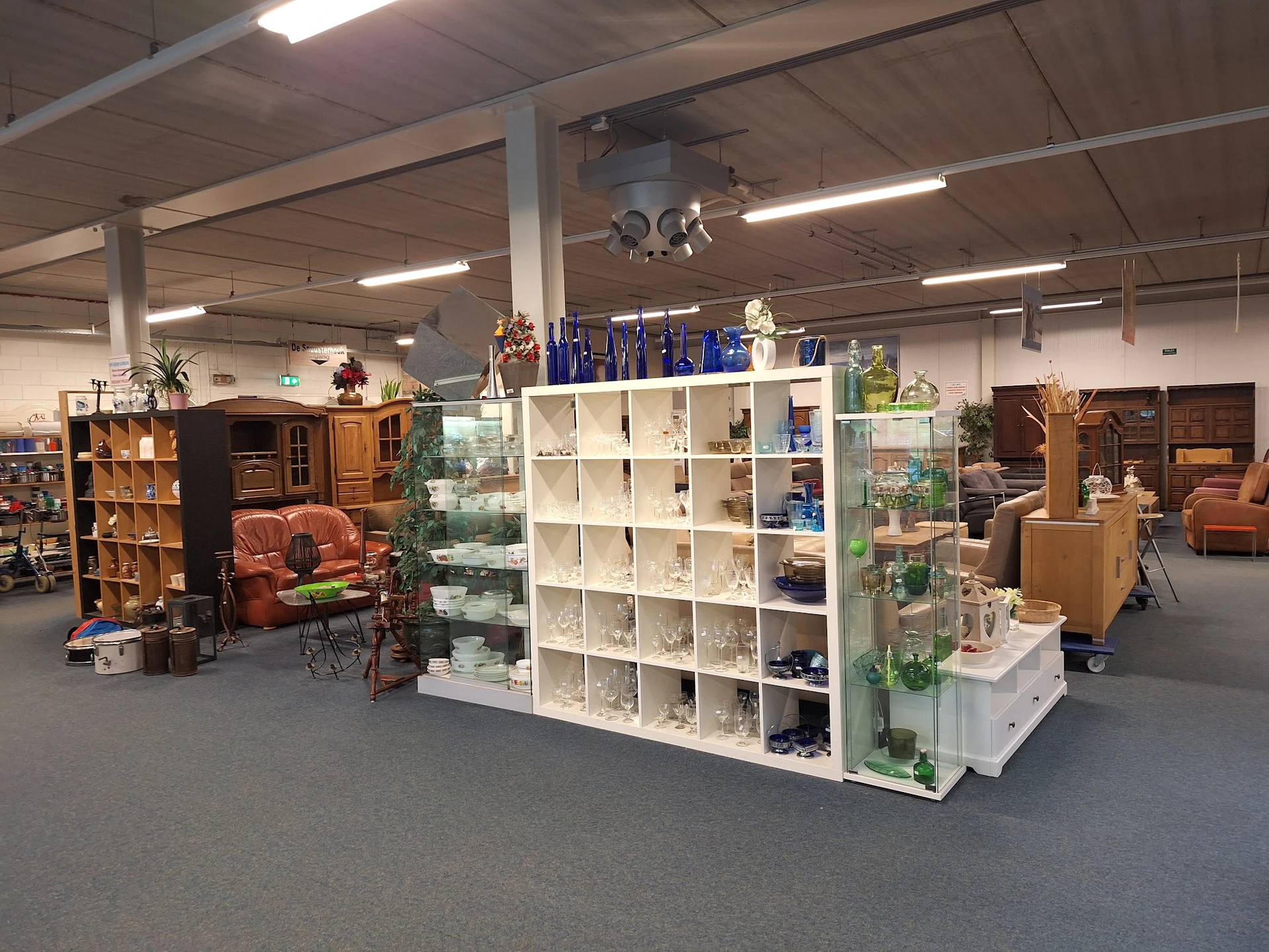 Winkelvloer met witte stellingen vol huishoudartikelen en decoraties, houten meubels en zithoeken op de achtergrond