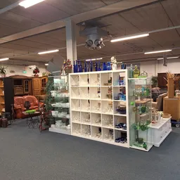 Winkelvloer met witte stellingen vol huishoudartikelen en decoraties, houten meubels en zithoeken op de achtergrond