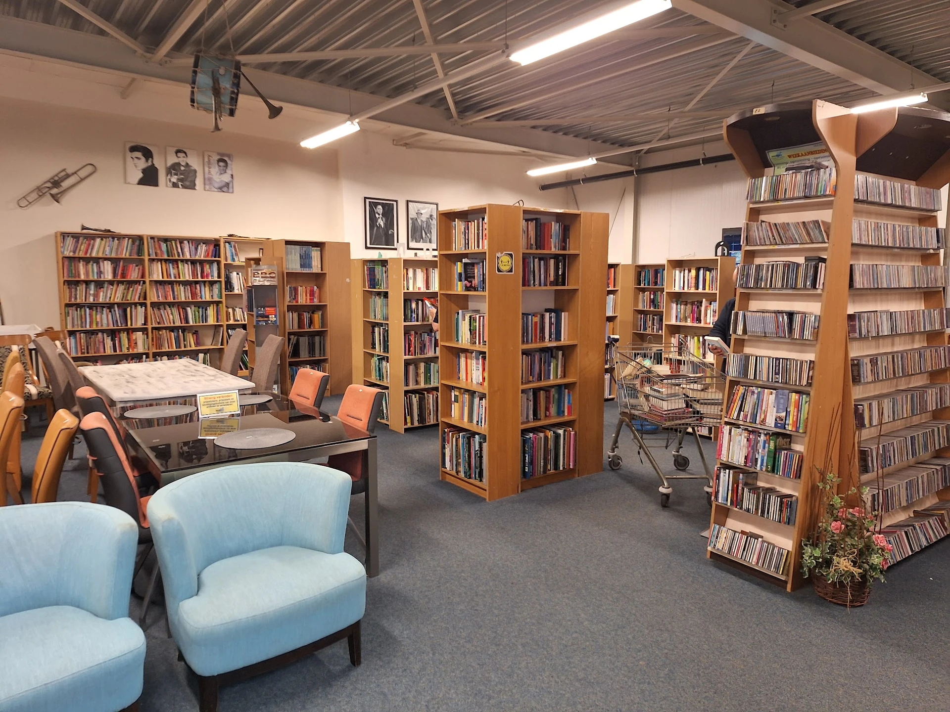Leesgedeelte van kringloopwinkel met boekenkasten, blauwe fauteuils en werktafels