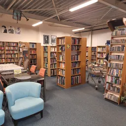Leesgedeelte van kringloopwinkel met boekenkasten, blauwe fauteuils en werktafels