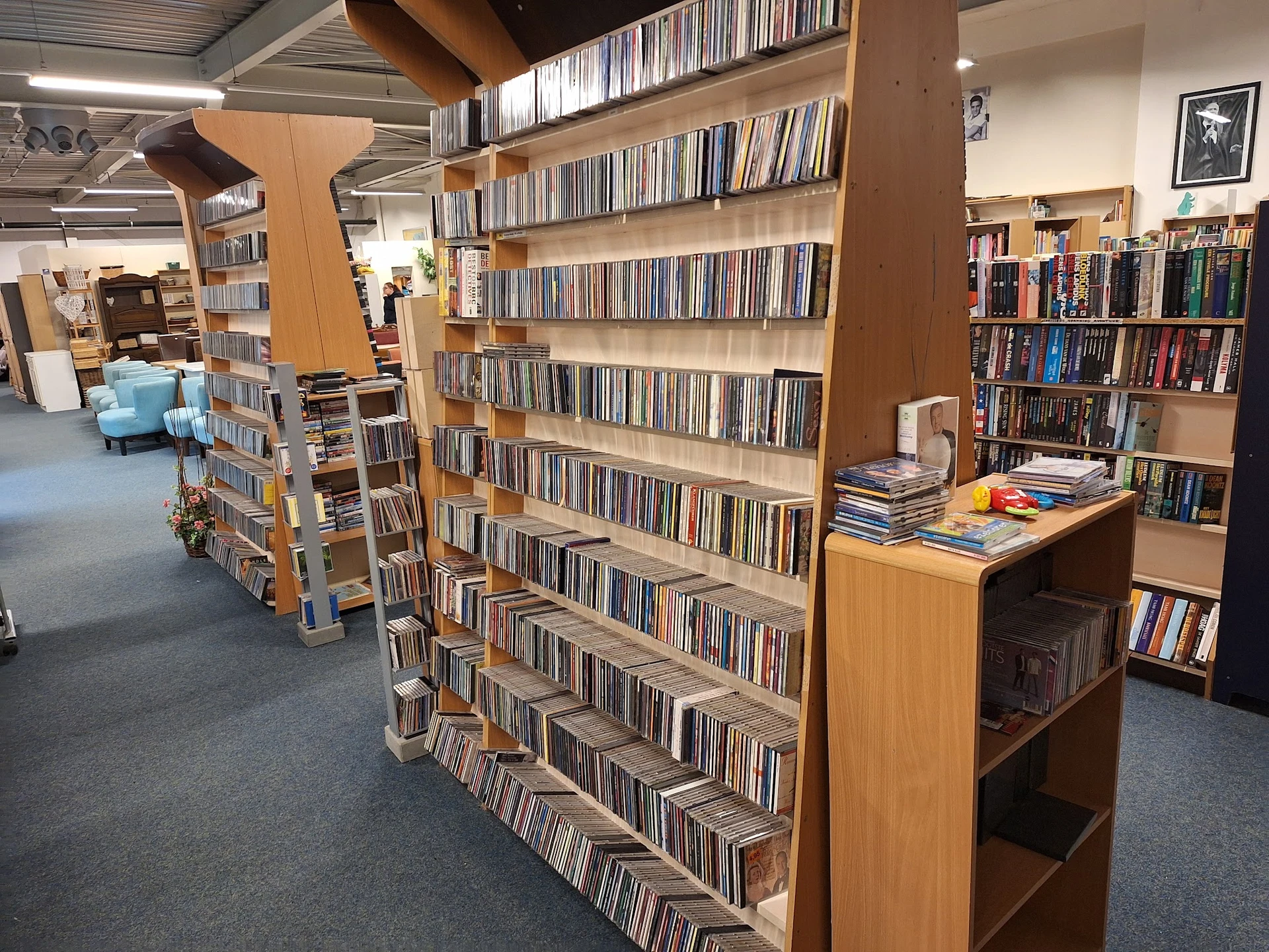 Winkelvloer met houten stellingen vol cd's en dvd's, blauwe zithoek op de achtergrond