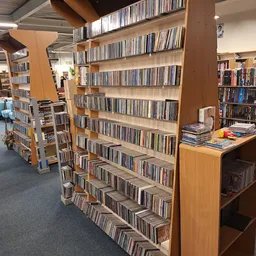 Winkelvloer met houten stellingen vol cd's en dvd's, blauwe zithoek op de achtergrond