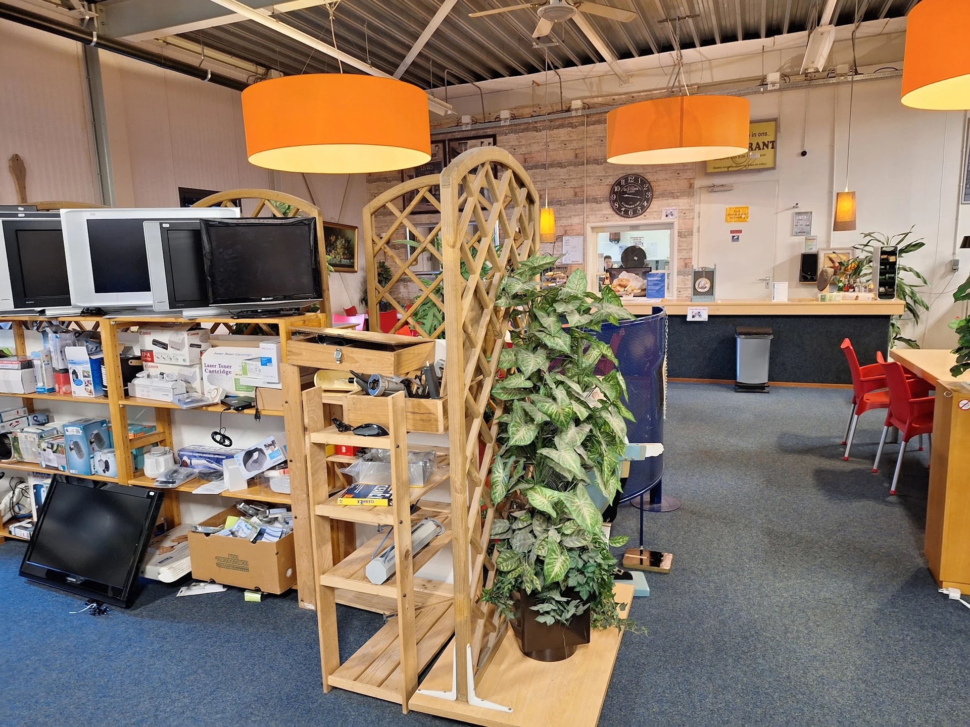 Winkelvloer met houten stellingen, groene plant in pot, oranje hanglampjes en diverse uitgestalde spullen