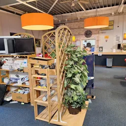 Winkelvloer met houten stellingen, groene plant in pot, oranje hanglampjes en diverse uitgestalde spullen