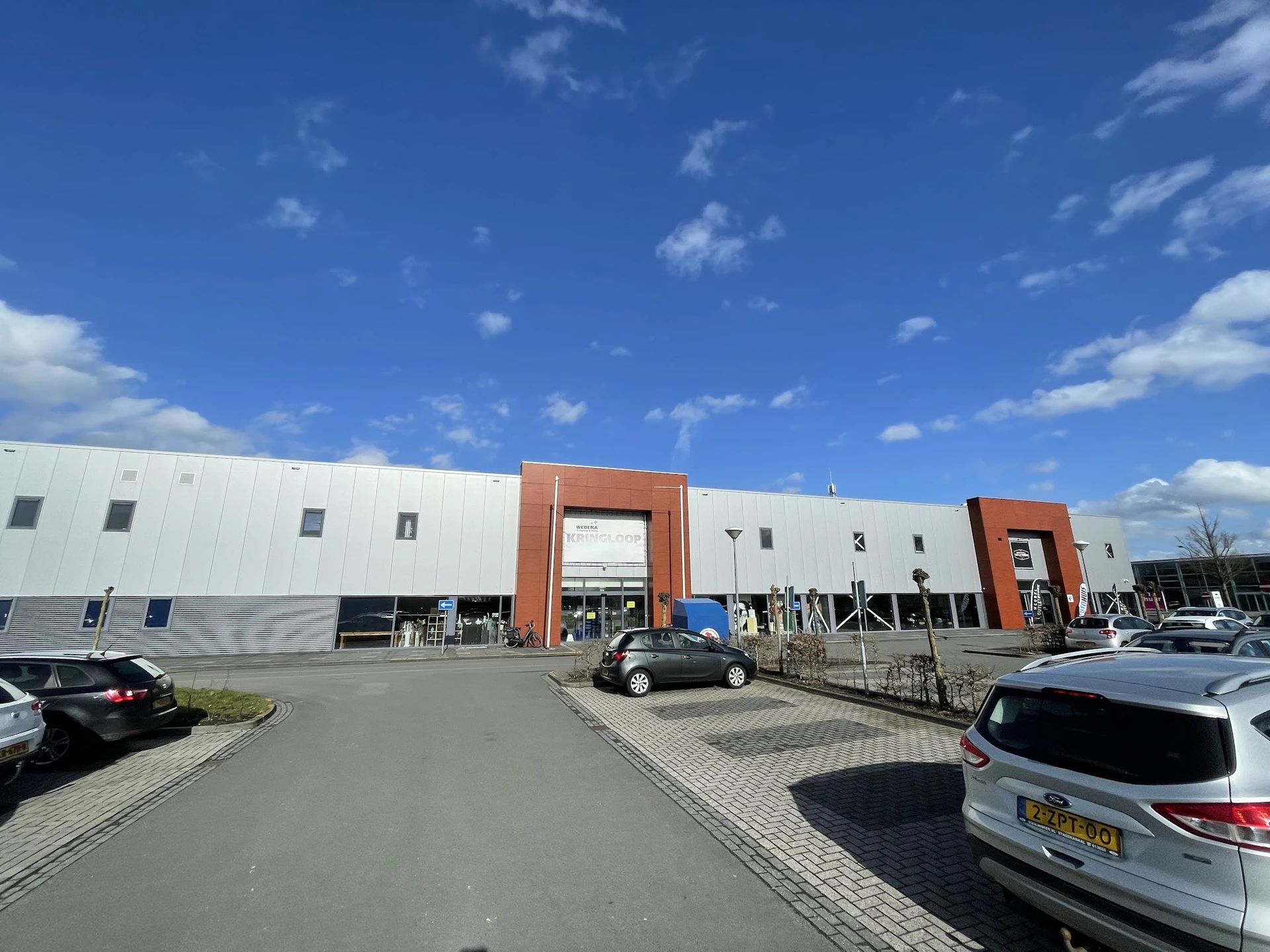 Exterieur van kringloopwinkel Wedeka met wit gebouw, oranje accenten en parkeerplaats