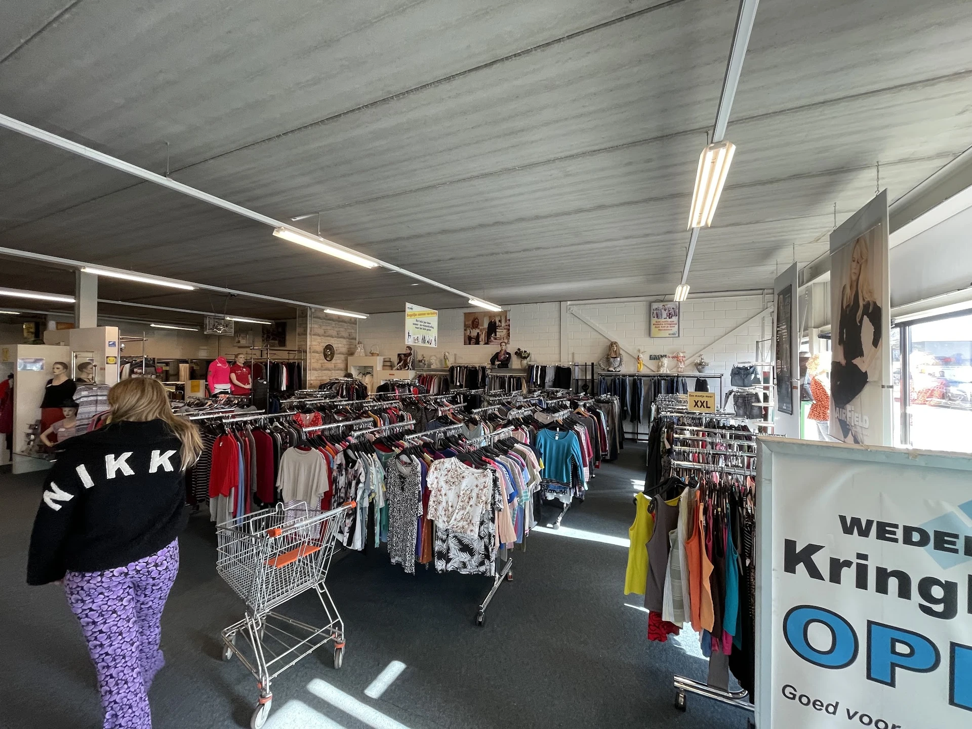 Winkelvloer met rekken vol tweedehands kleding, winkelwagens en verlichting van bovenaf