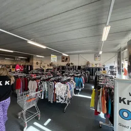 Winkelvloer met rekken vol tweedehands kleding, winkelwagens en verlichting van bovenaf