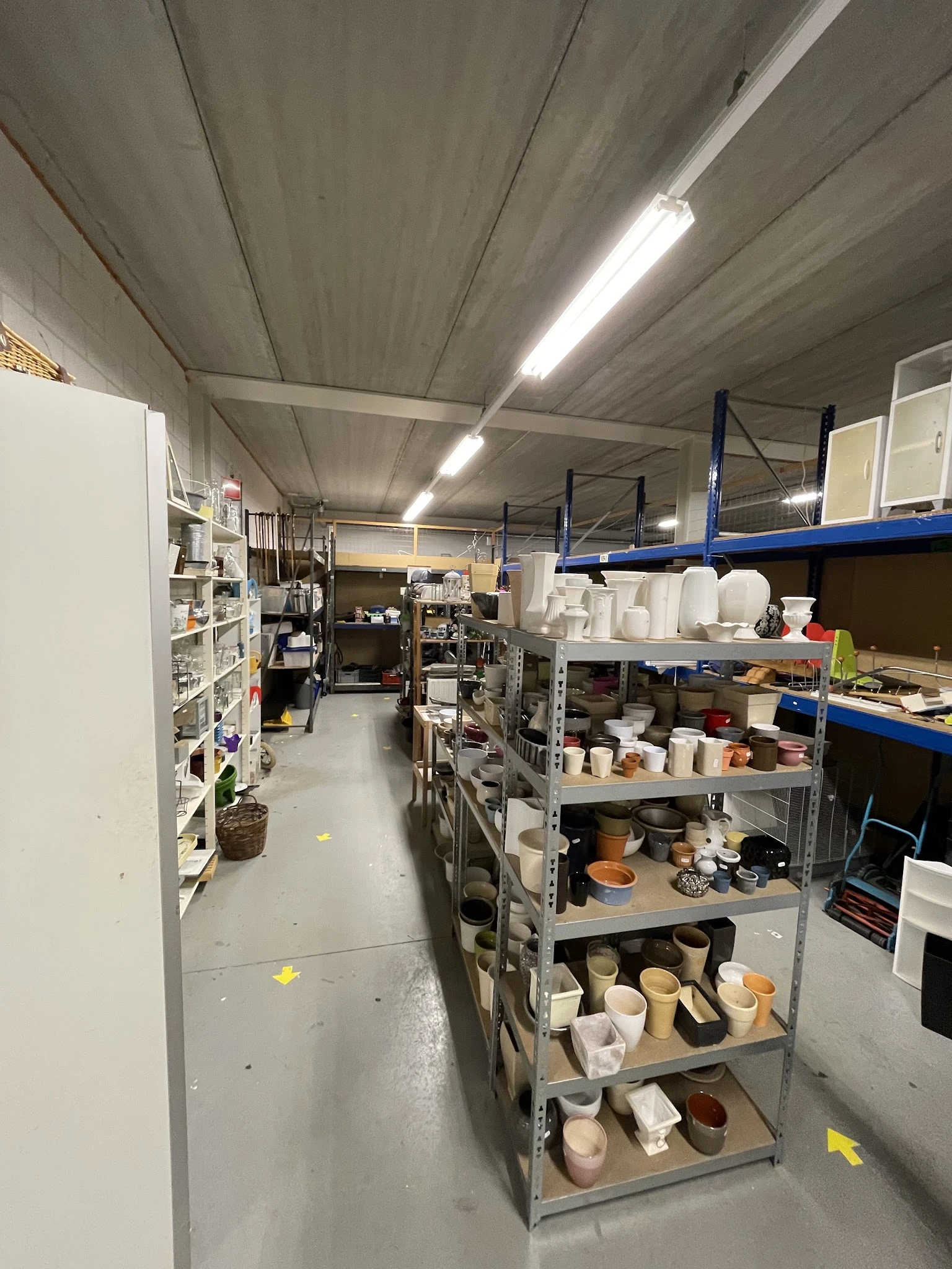 Winkelinterieur met stellingen vol huishoudelijke artikelen, potten en serviesgoed in kringloopwinkel