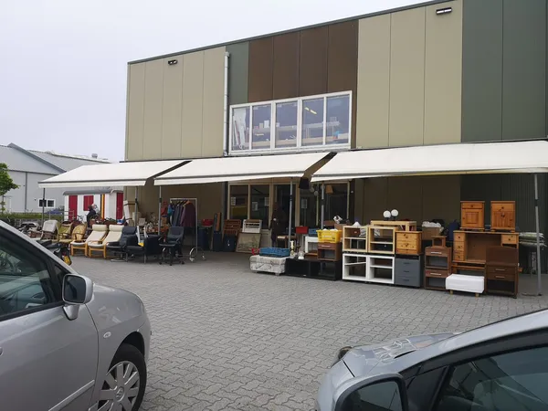 Voorkant van kringloopwinkel met overkapping, stellingen met meubels en spullen buiten uitgestald