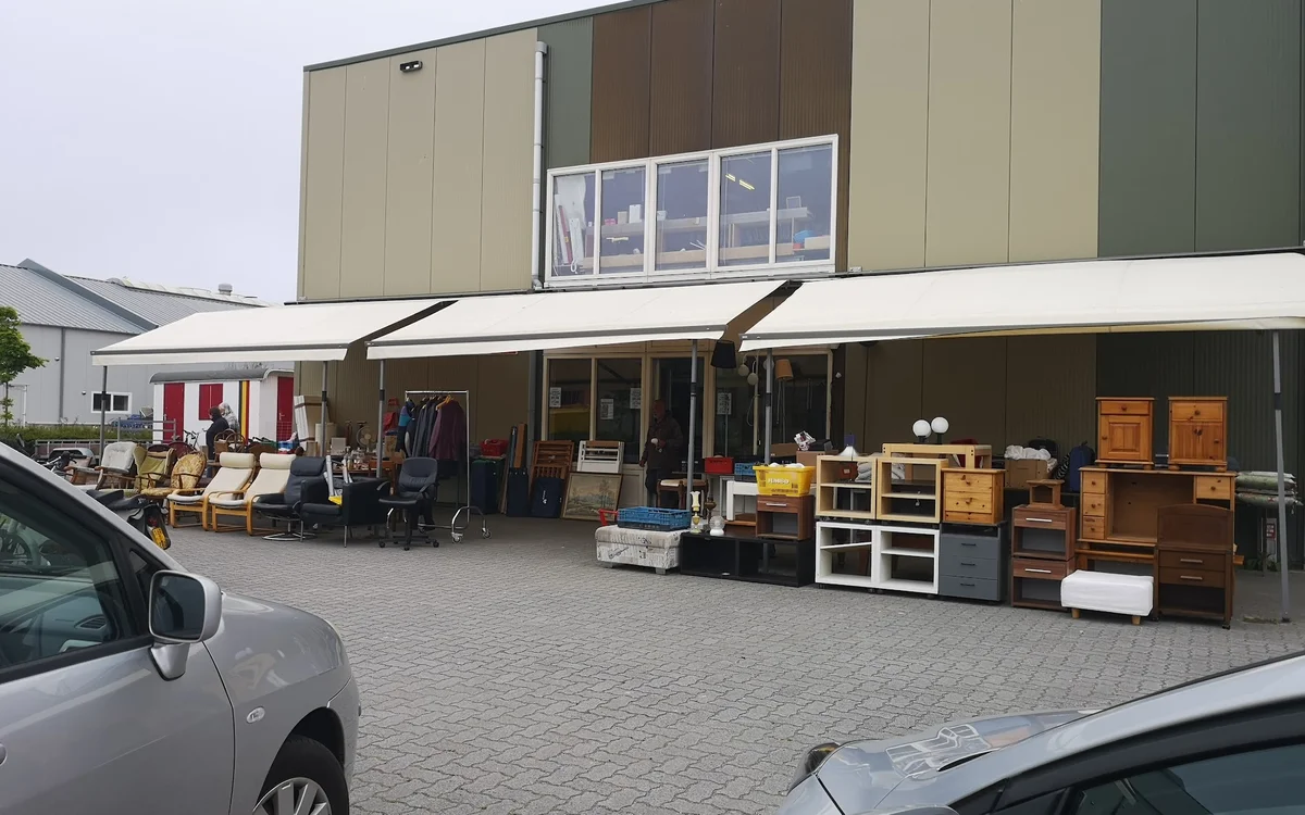 Voorkant van kringloopwinkel met overkapping, stellingen met meubels en spullen buiten uitgestald