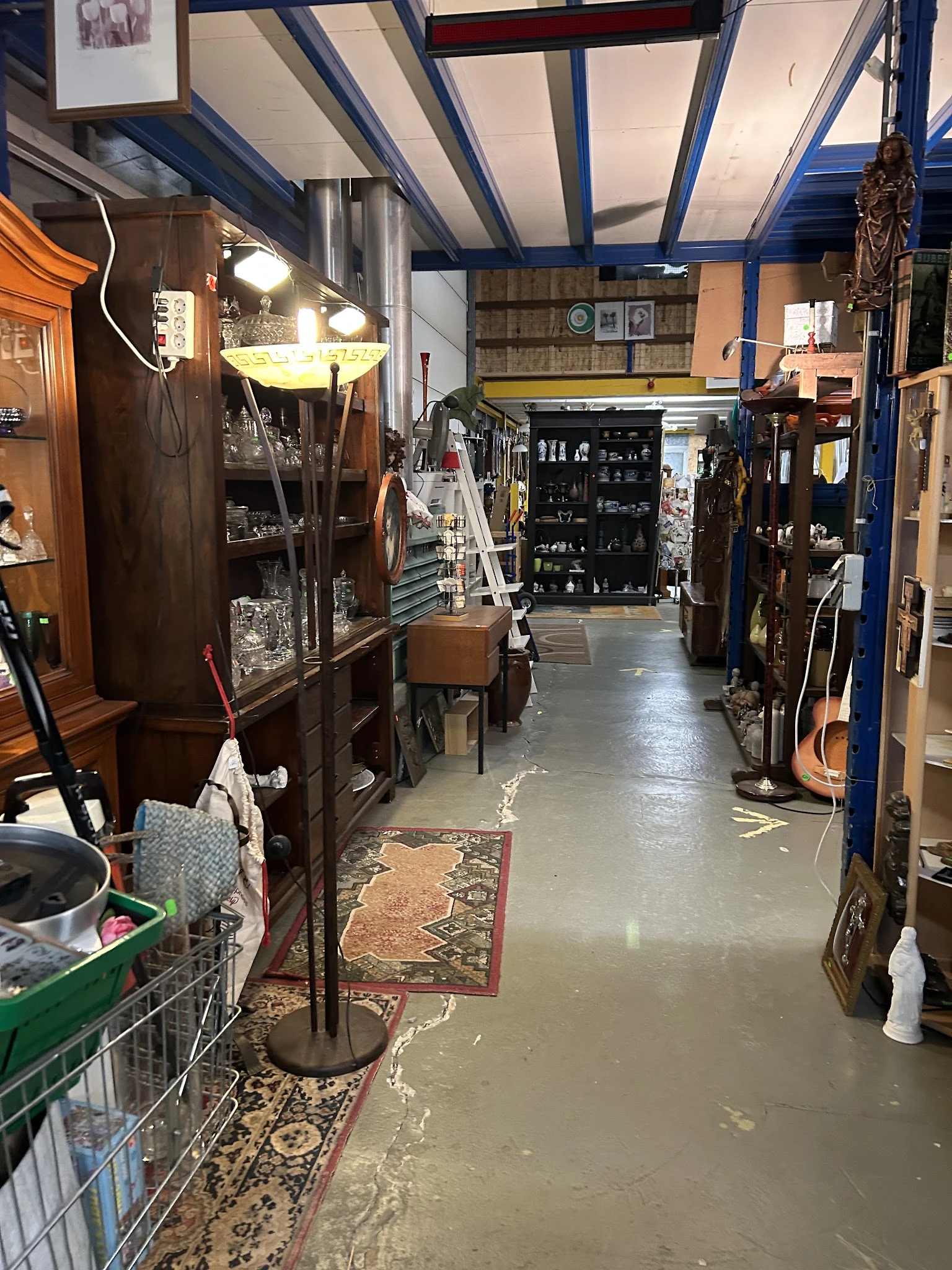 Binnenaanzicht van kringloopwinkel met stellingen, meubels, instrumenten en diverse spullen langs beide zijden