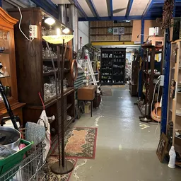 Binnenaanzicht van kringloopwinkel met stellingen, meubels, instrumenten en diverse spullen langs beide zijden