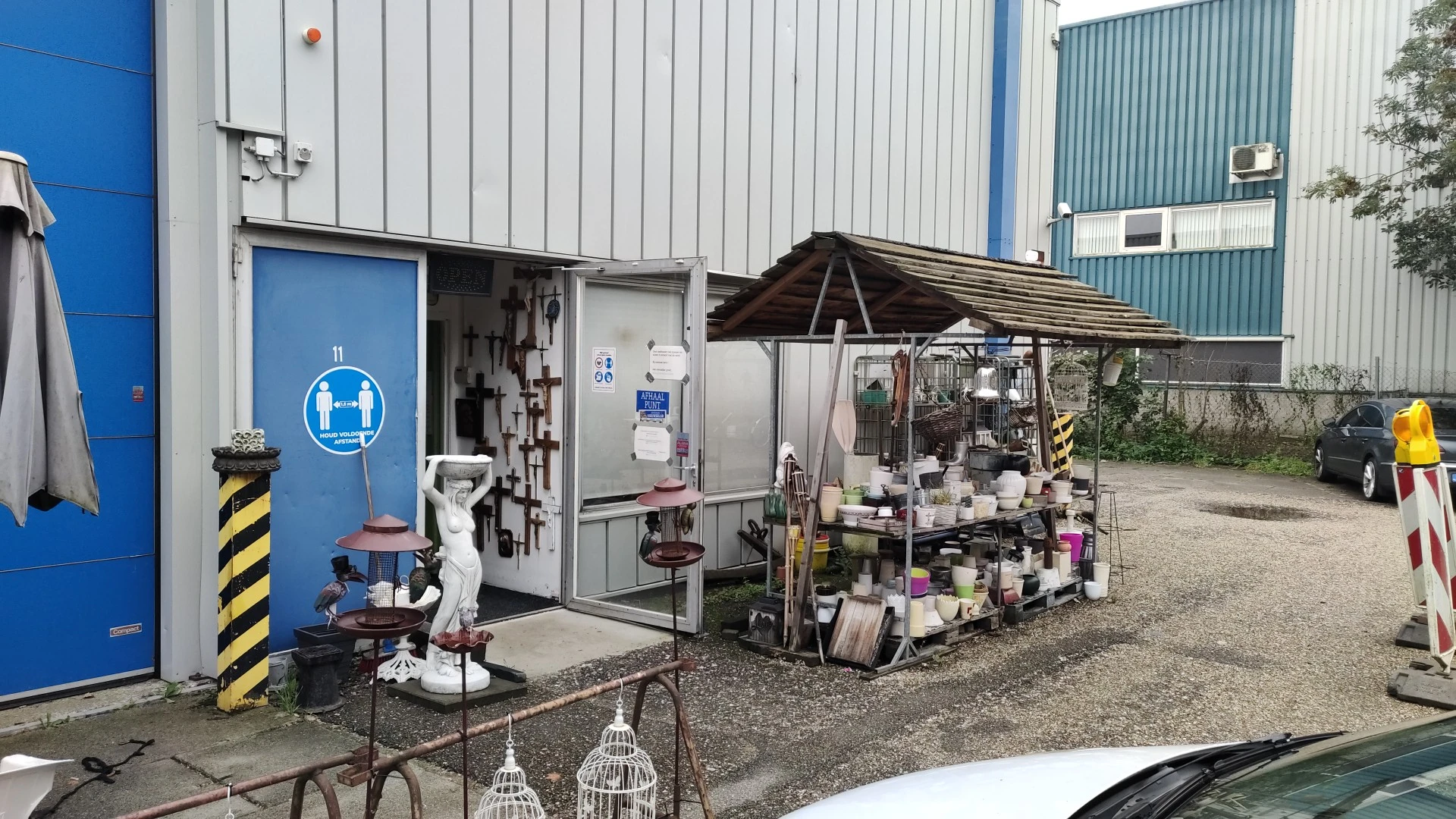 Exterieur van kringloopwinkel met blauwe deur en stellingen met spullen buiten