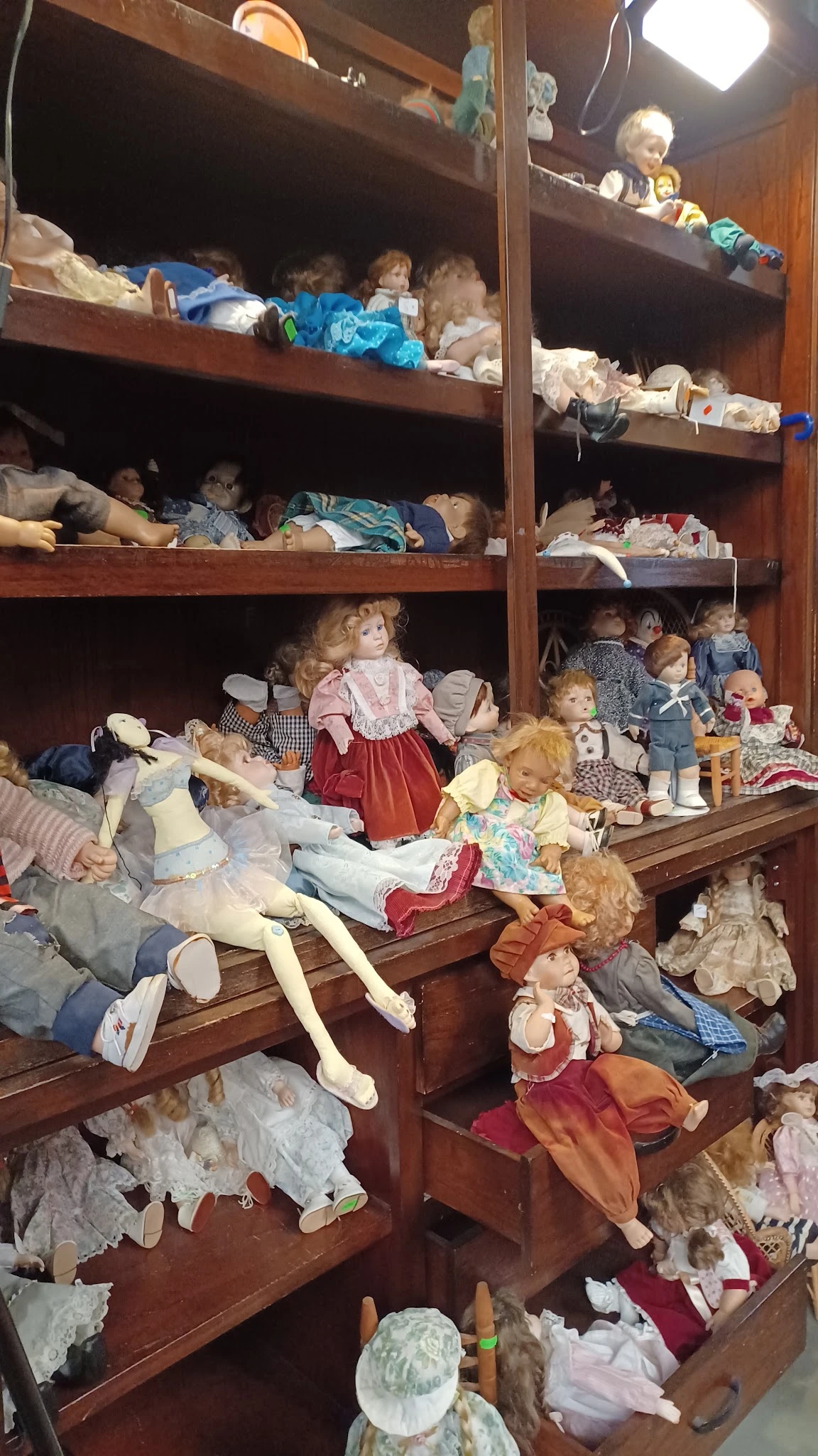 Houten vitrinekast vol met verzameling poppen en speelgoed in verschillende kleding en stijlen