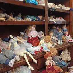 Houten vitrinekast vol met verzameling poppen en speelgoed in verschillende kleding en stijlen