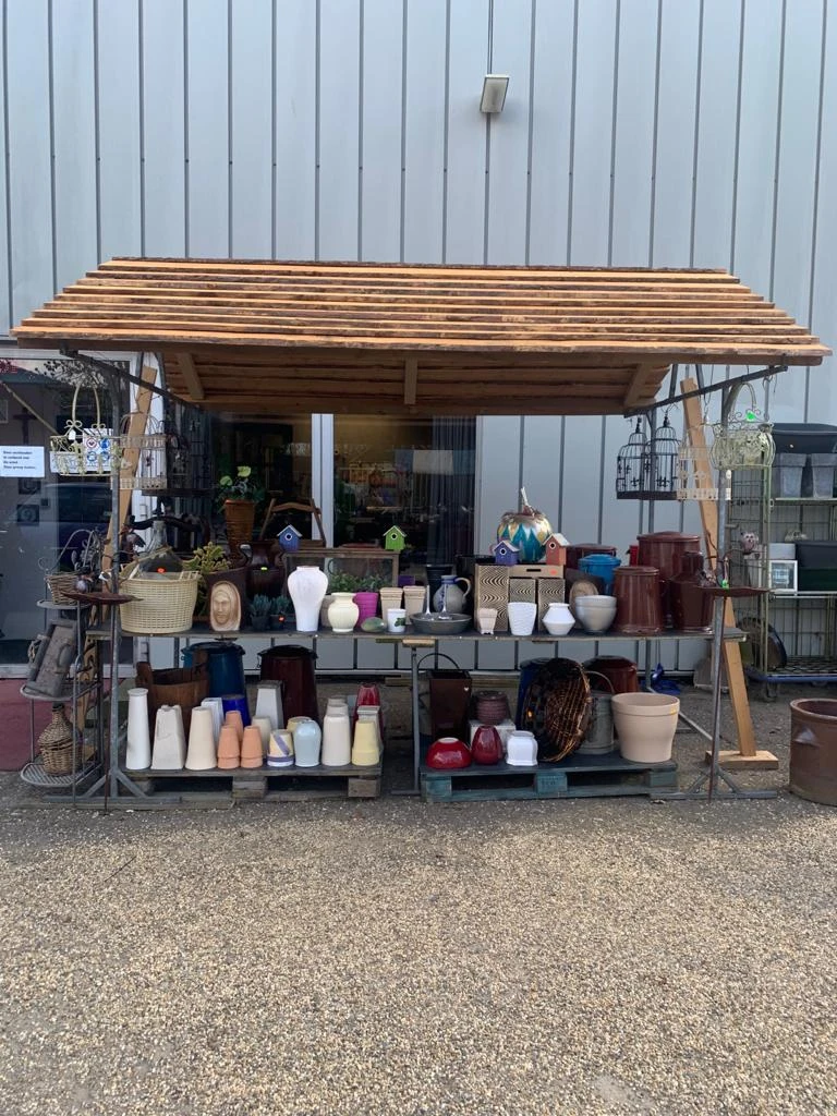 Uitgestalde huishoudartikelen en decoratie onder een houten afdak buiten de winkel