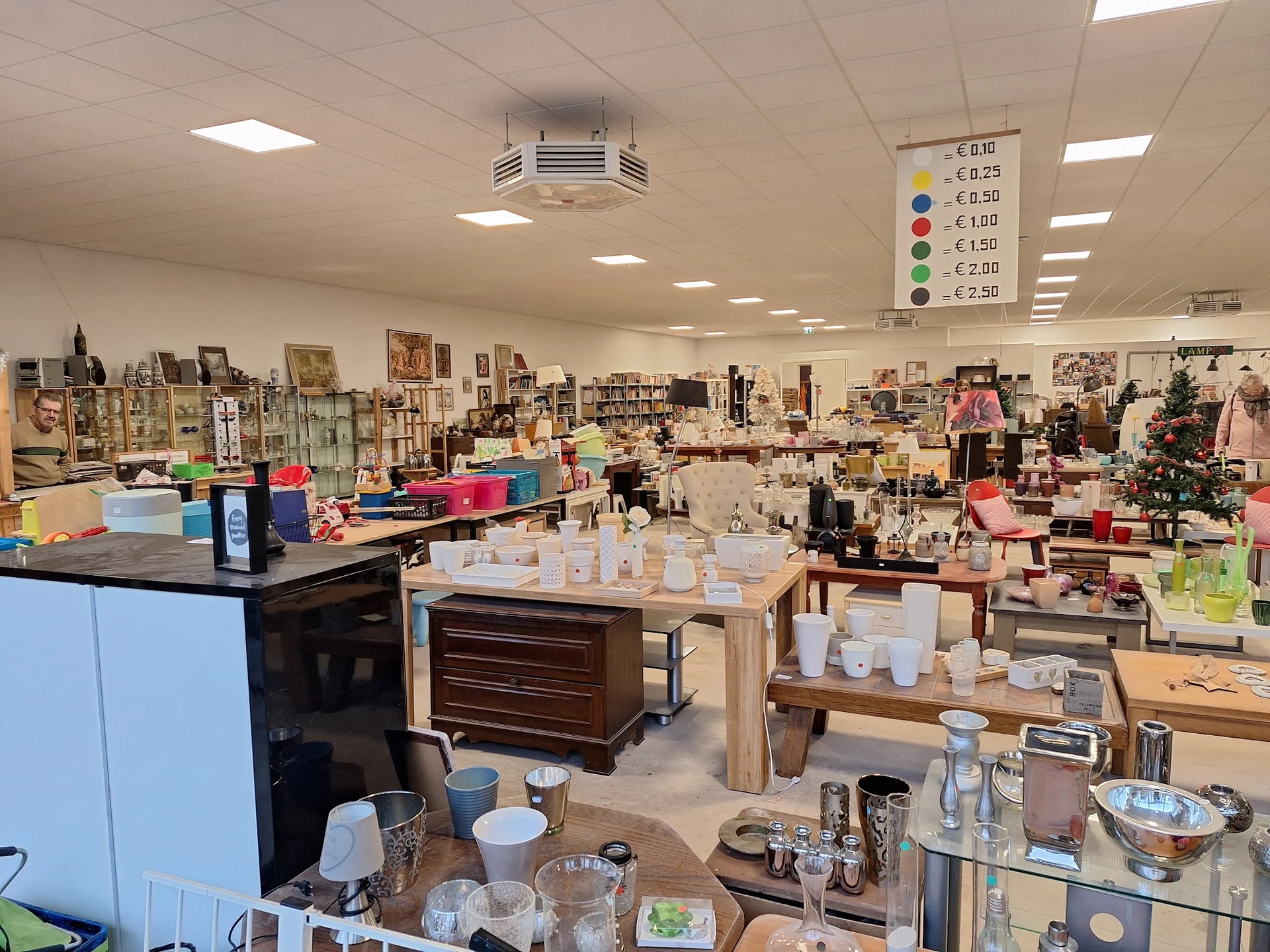 Overzicht van de winkelvloer met diverse gebruiksartikelen, serviesgoed en decoratieve spullen op tafels en stellingen