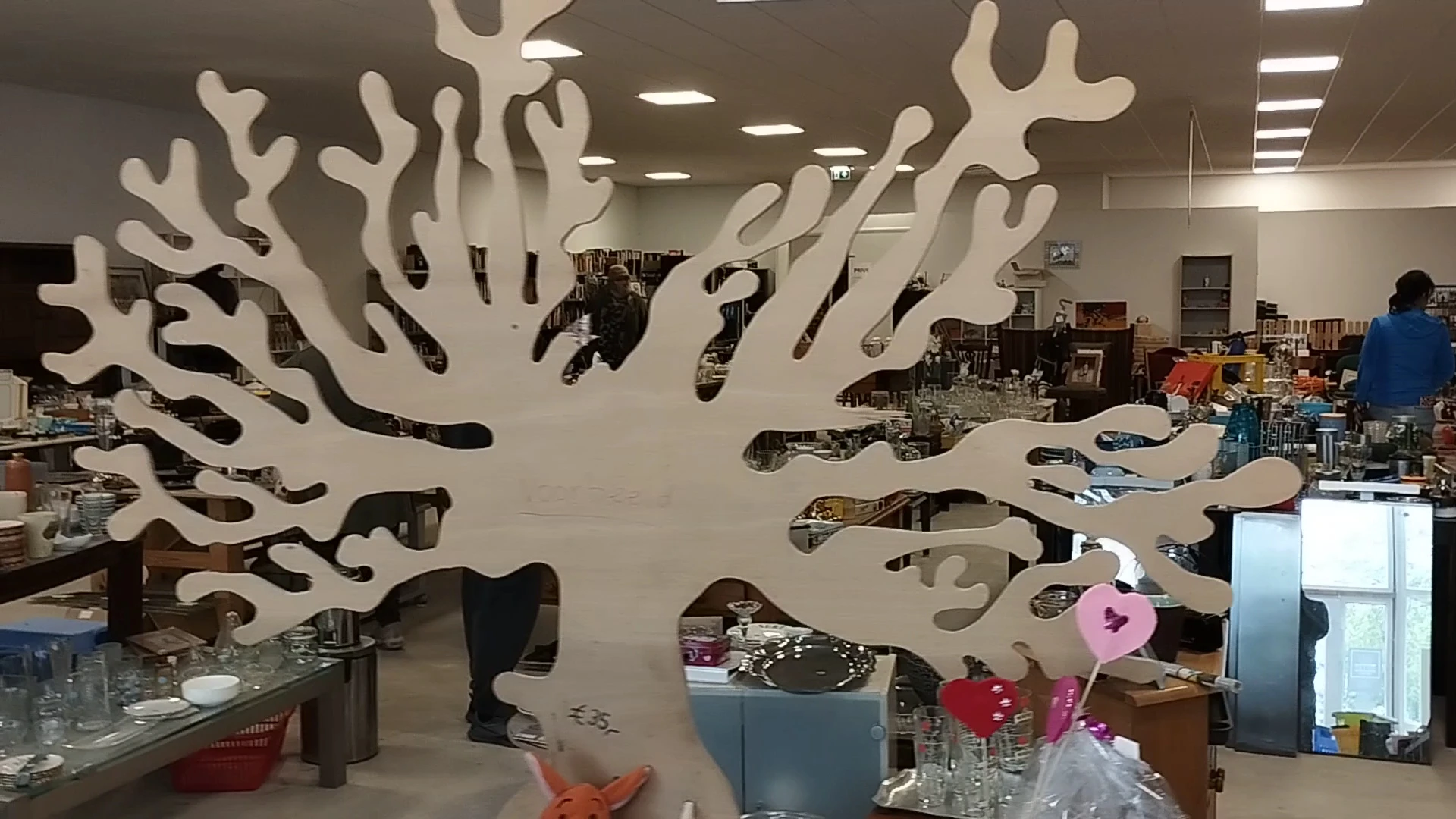 Winkelvloer met decoratief kunstwerk van witte takken aan muur en diverse spullen in kringloopwinkel