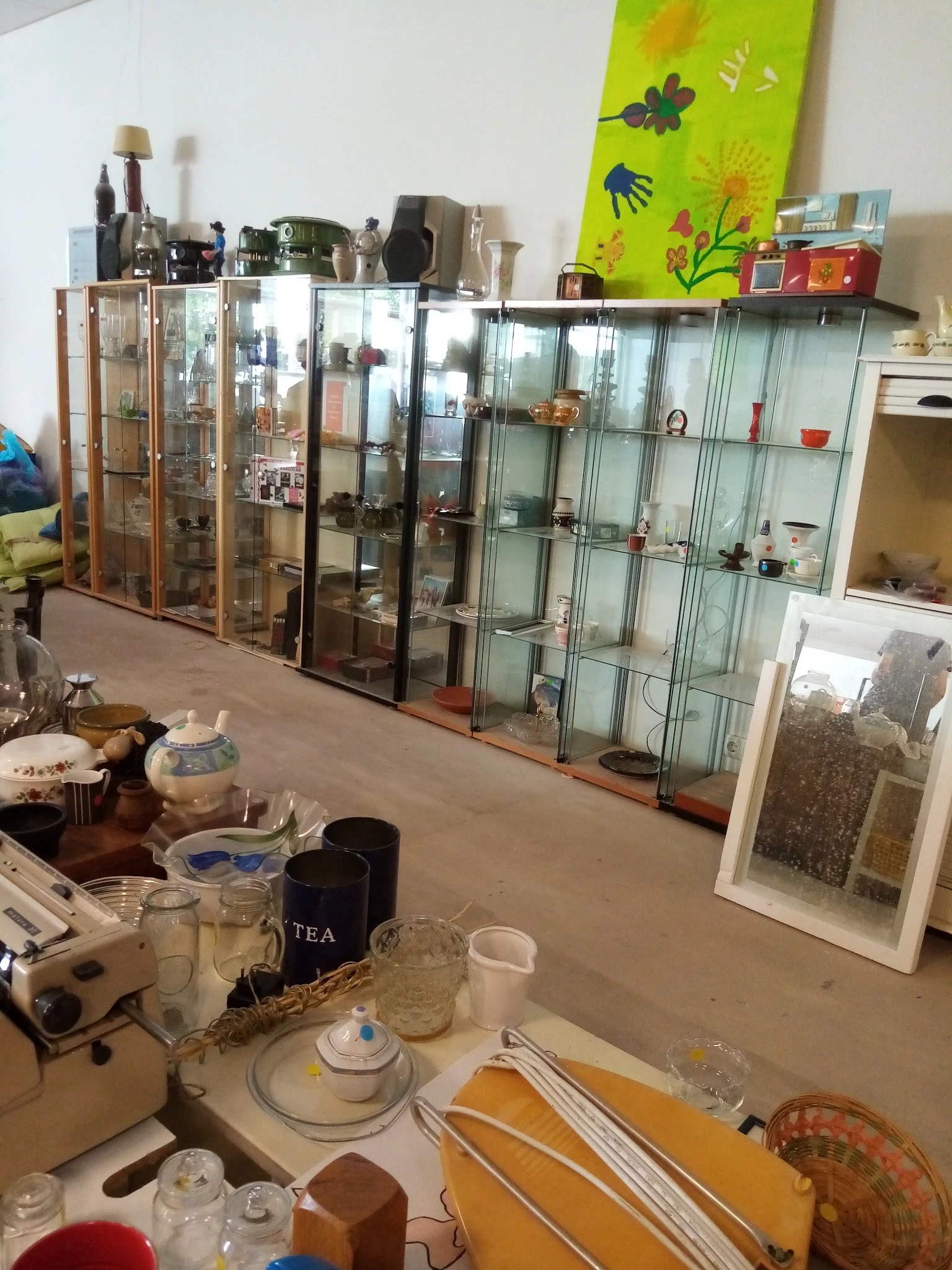 Kringloopwinkel interieur met glazen vitrinekasten vol verzamelde spullen en servies op de voorgrond