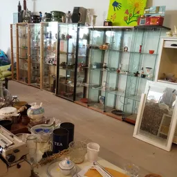 Kringloopwinkel interieur met glazen vitrinekasten vol verzamelde spullen en servies op de voorgrond