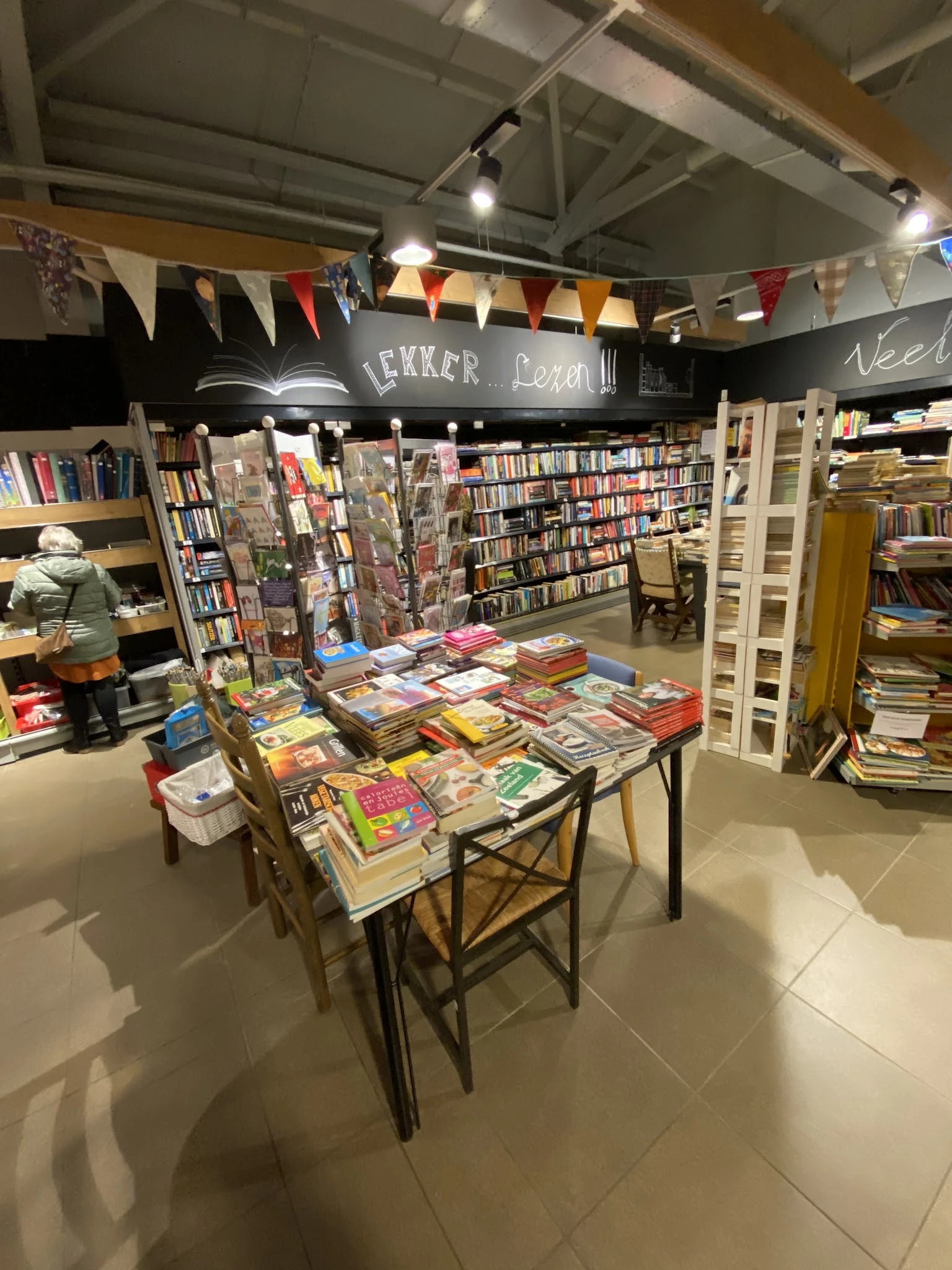 Tafels met uitgestalde tweedehands boeken en dvd's in de winkel, omgeven door kasten met verder aanbod