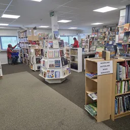Binnenaanzicht van een kringloopwinkel met boekenkasten, displaykasten en klanten tussen de stellingen