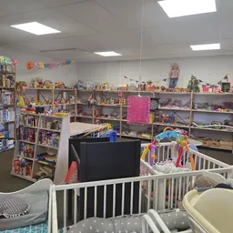 Kringloopwinkel met speelgoed, boeken en babyspullen op stellingen en in witte kinderbedjes op de vloer